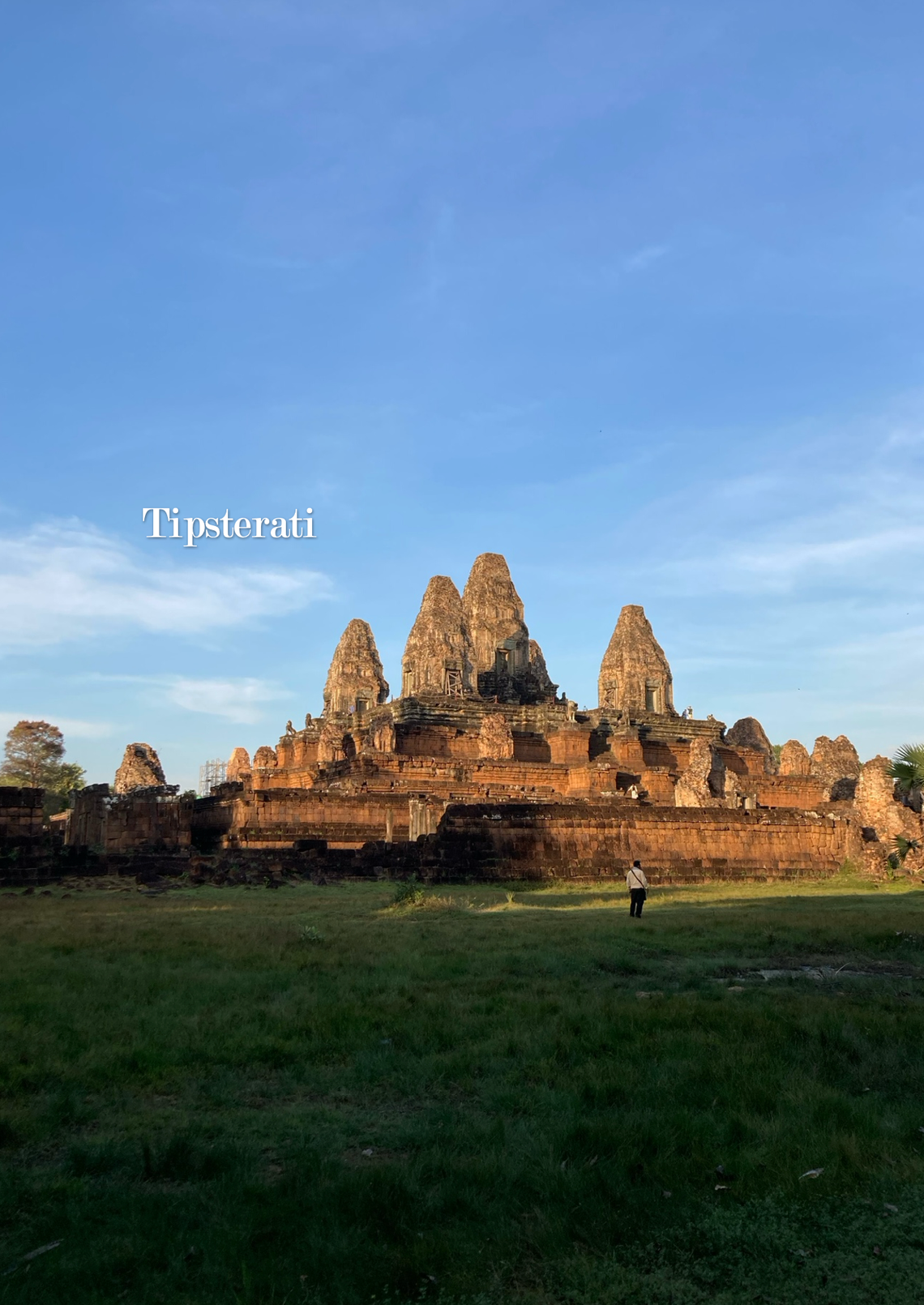 The stupas of Pre Rup against a blue sky with a small figure in the distance looking at the temple