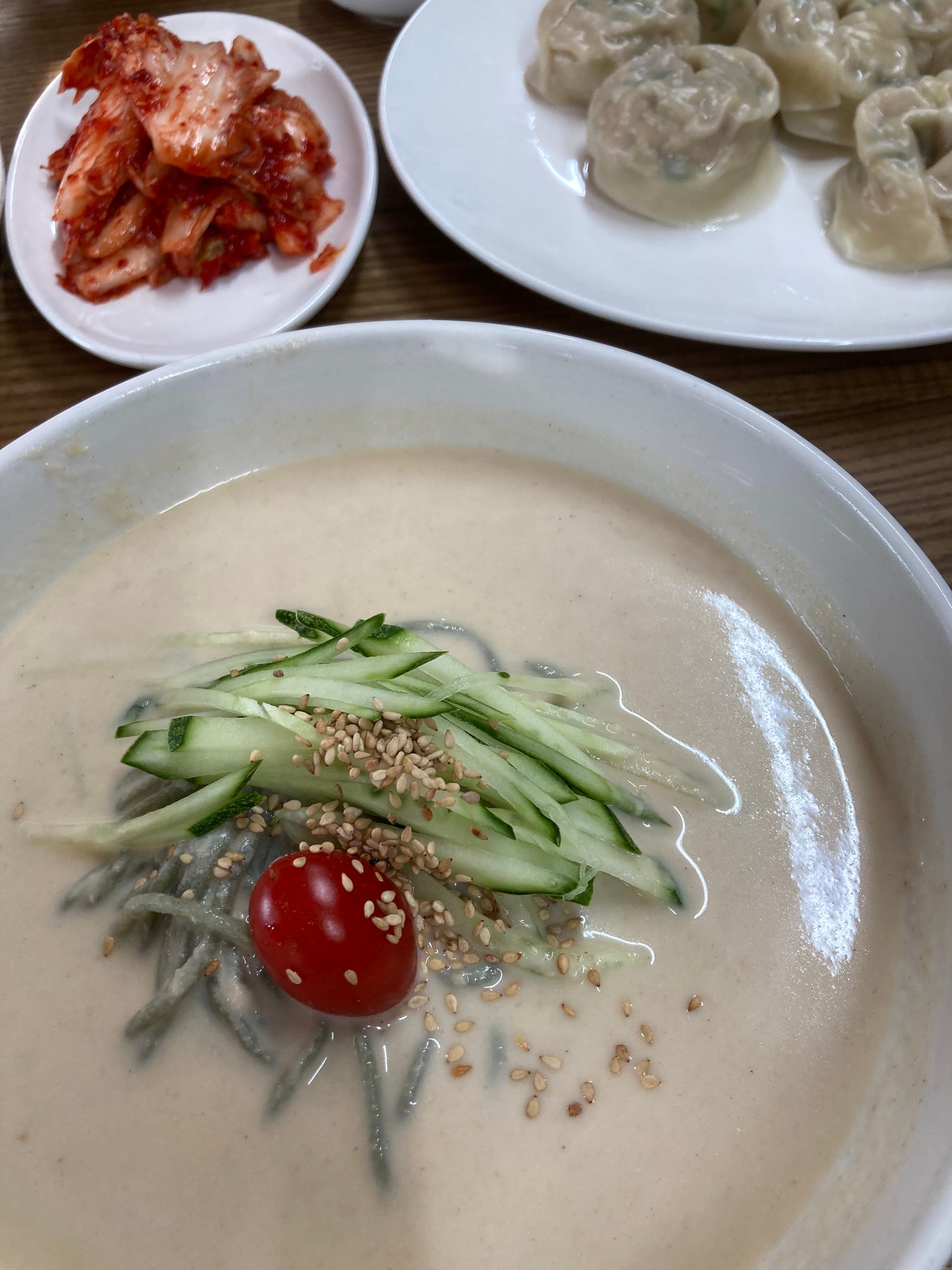 A close up of a bowl of soy bean noodles garnished with cucumber slices, a cherry tomato and sesame seeds.