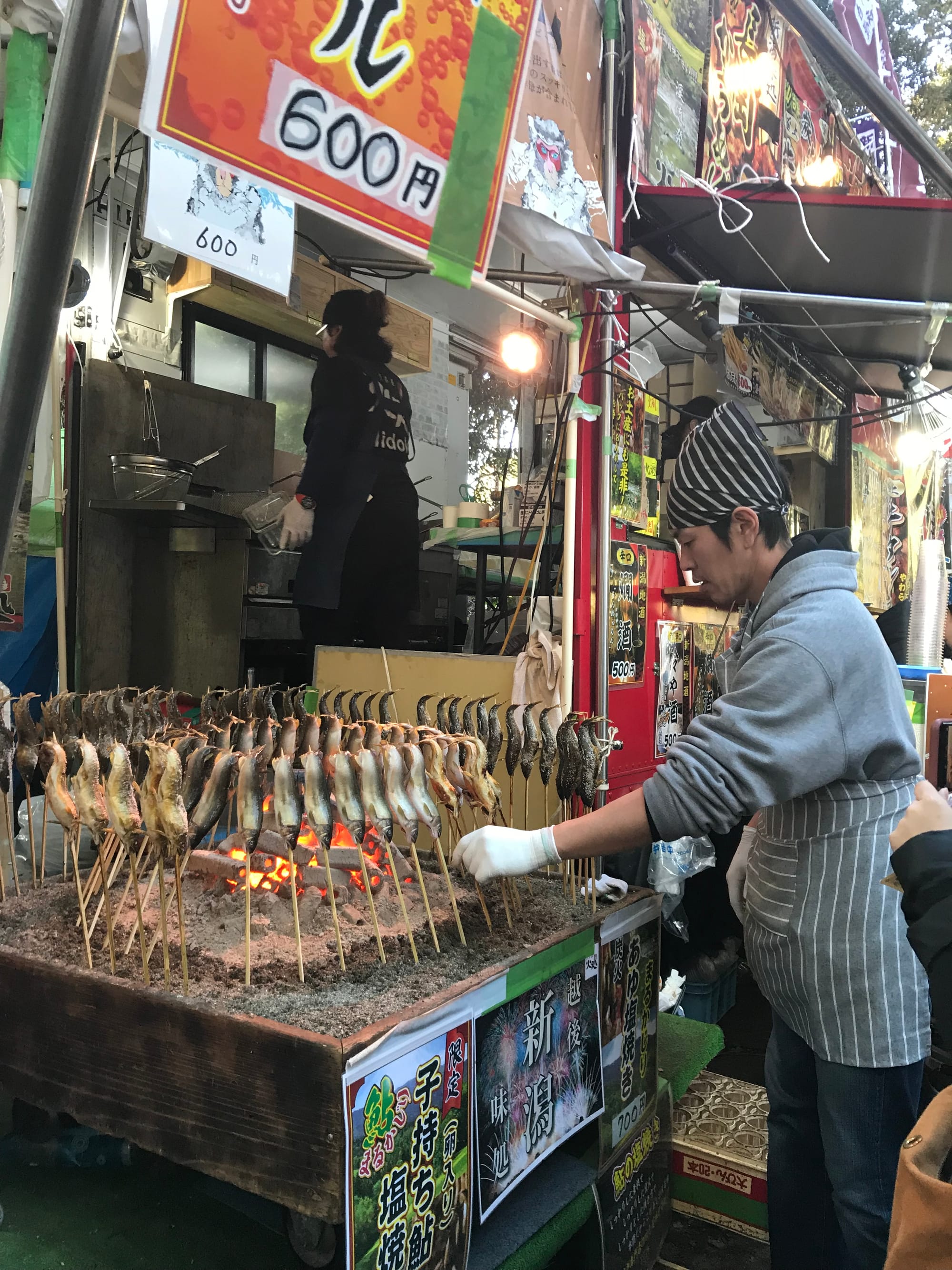 A man tends to grilled fish on skewers at a street stall