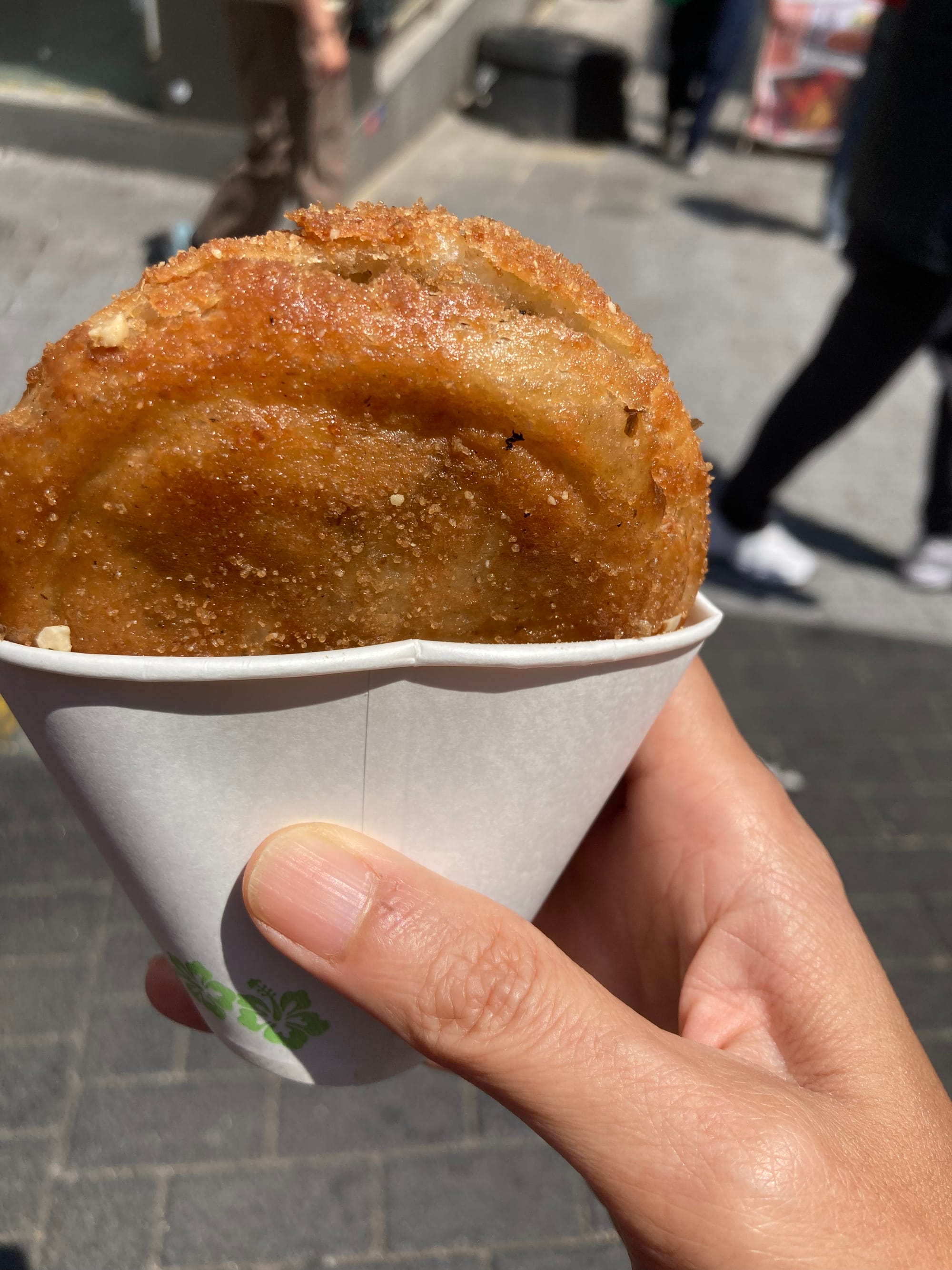 A ssiak hotteok–round, golden, and crisp–in a paper cup.