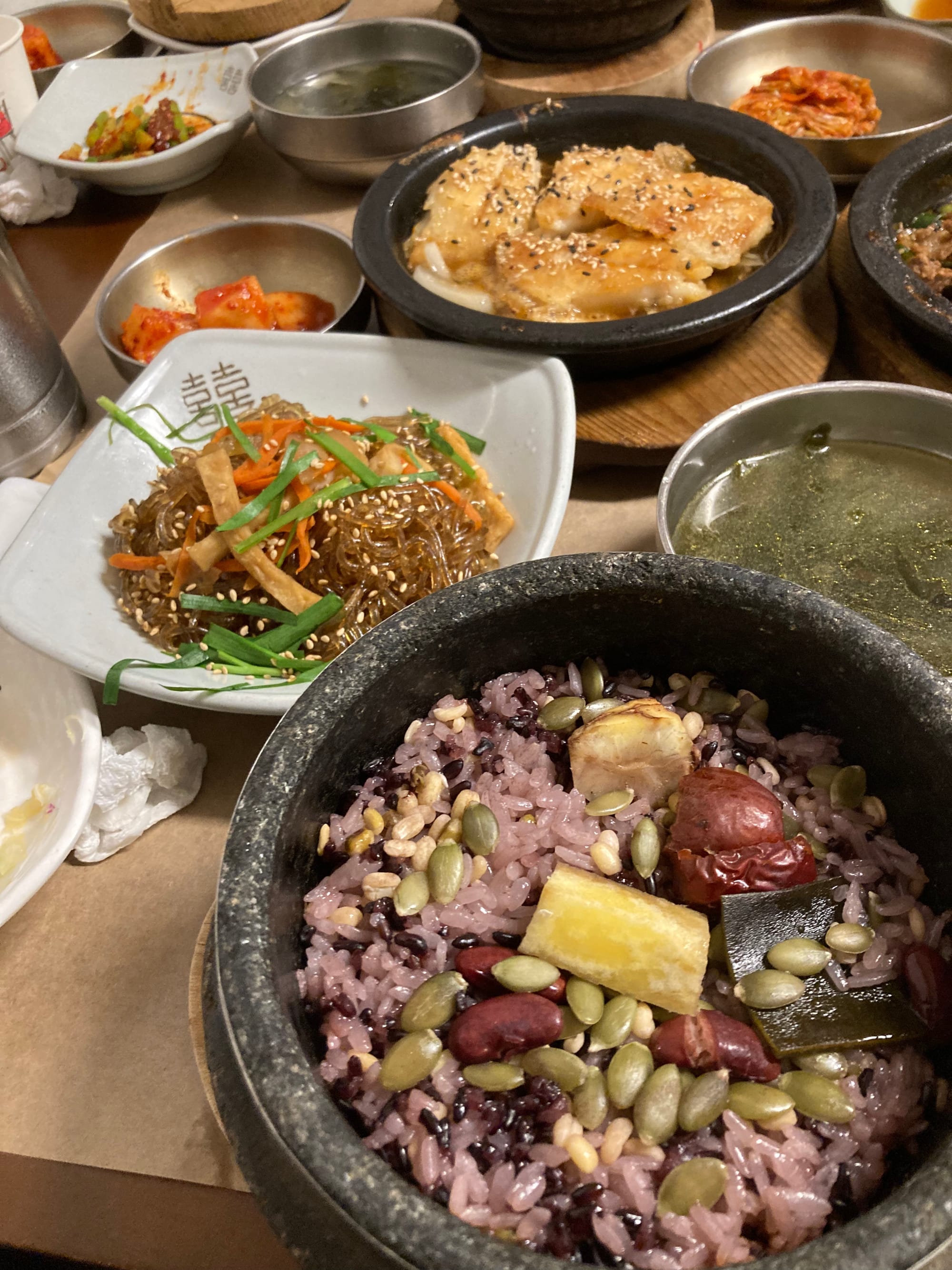 An array of small plates of Korean food (rice, japchae, kimchi, soup, braised fish) on a table