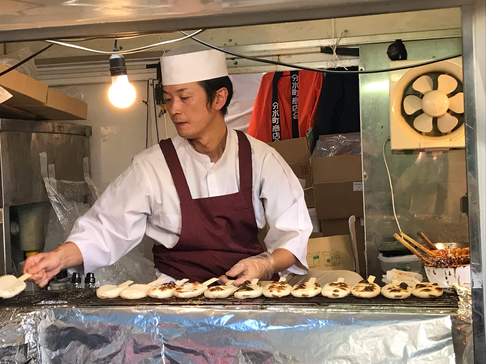 A man grills mochi on skewers in a food truck