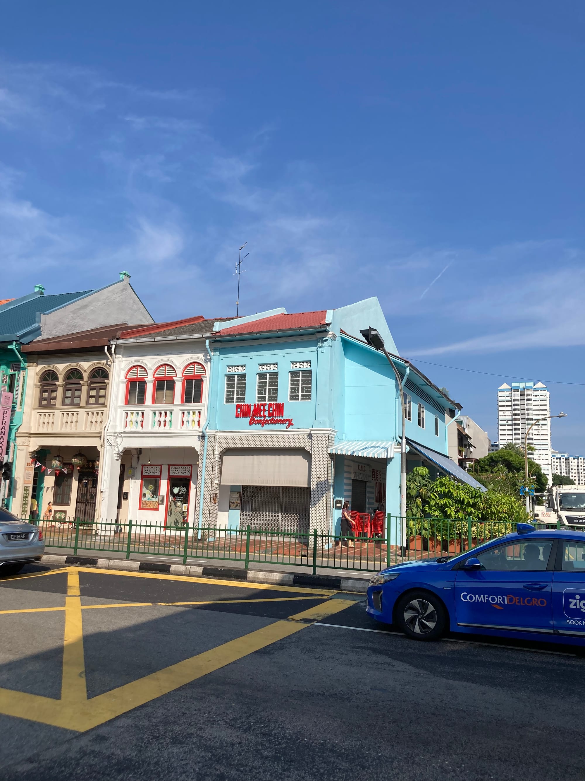 A row of colourful two-storey shop houses with a busy road before it.