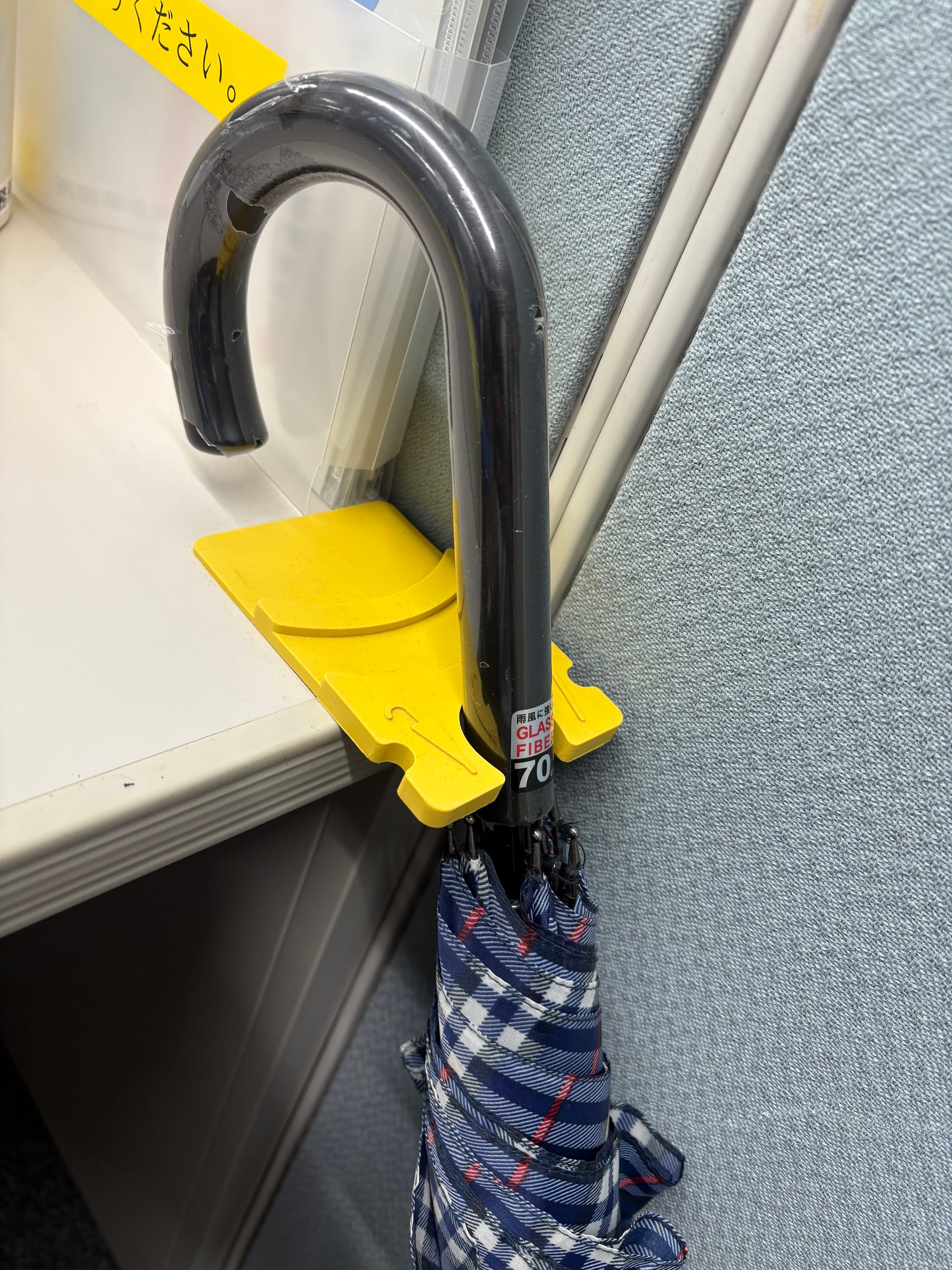 A yellow plastic holder with a notch is affixed to the edge of a desk and holds an umbrella.