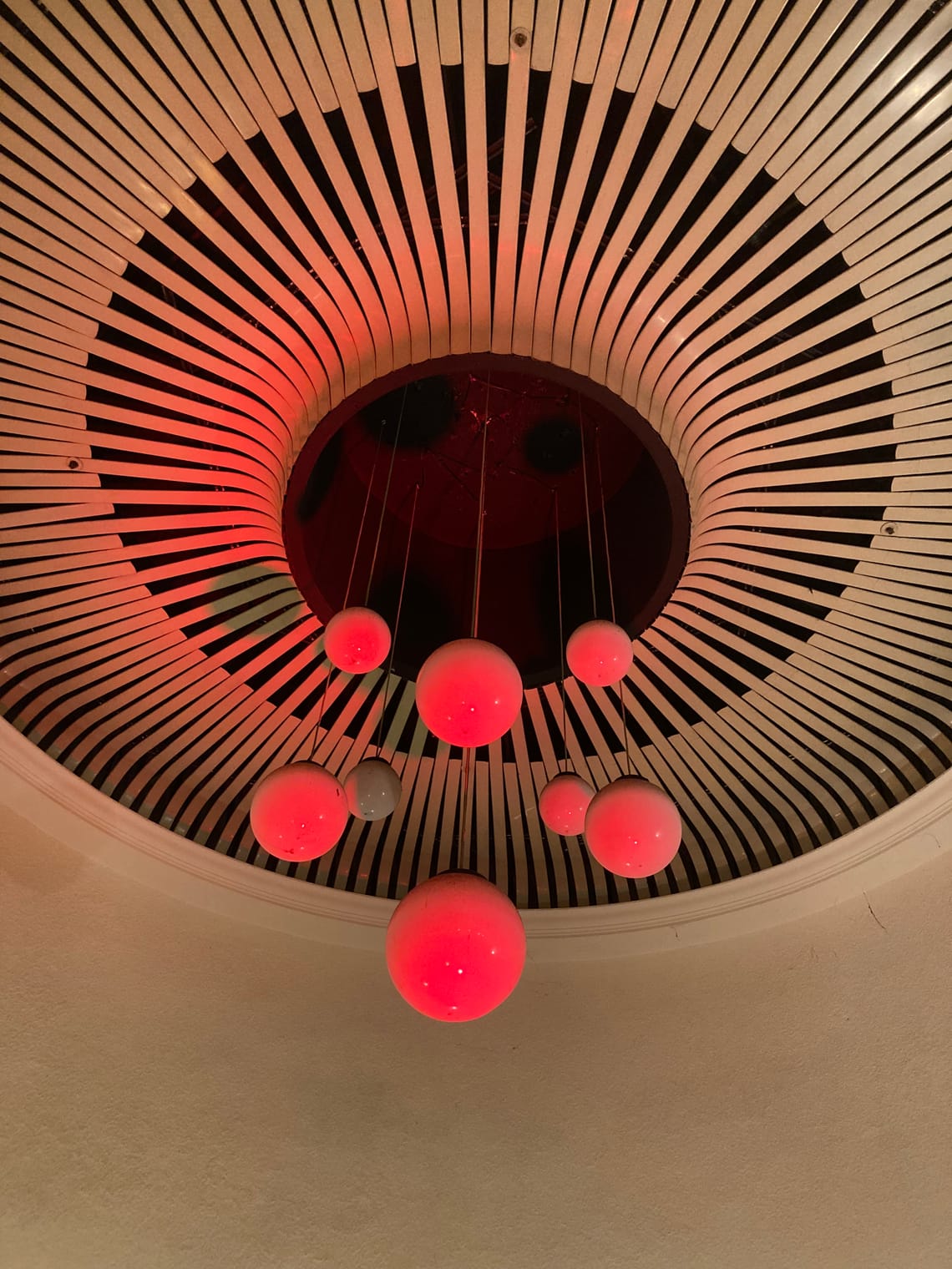 Eight different sized red glass balls hang from a ceiling painted black and white