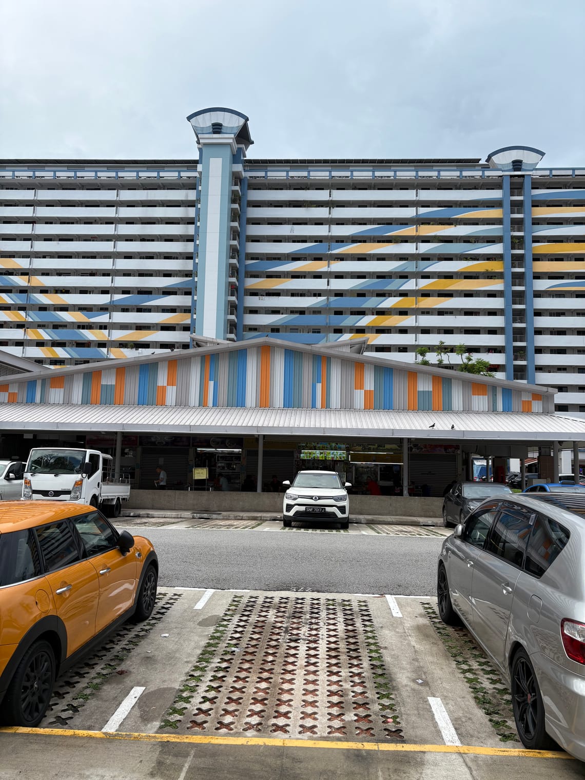 Cars in the foreground, with a low level market building in the middle ground and a tall block of flats behind.